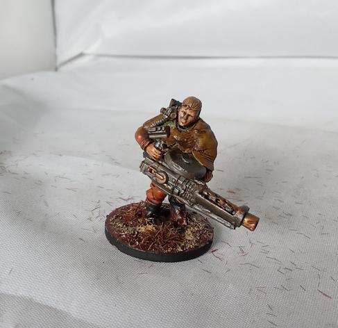 An infantry model in an orange jumpsuit, and rags. She has brown hair, a gasmask stowed on her right shoulder, and a very large gun.