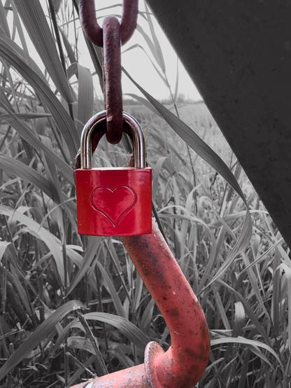 Hintergrund des Bildes ist schwarz weiß. Es sticht nur die Farbe rot hervor. Ein Schloss mit einem Herzsymbol ist an den Überresten einer Konstruktion befestigt.
