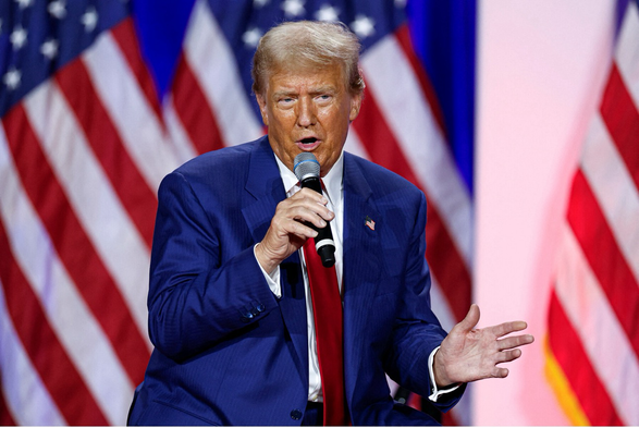 The Former Guy riffs onstage at a rally in 2024 with a goofy face and a dance posture, his face very bronzed/orange except around the beady eyes. He sports the usual clownish long red tie and is surrounded by American flags. AP photo.