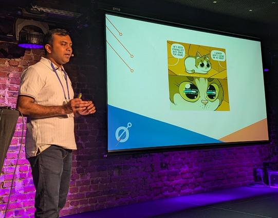 Tom next to a meme slide with a cat looking at a (very slow?) firmware update progress bar.