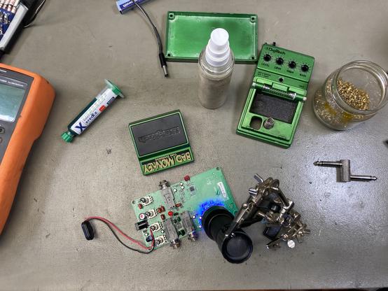 A Bad Monkey guitar effect pedal in pieces on my workbench with a UV light curing some new solder mask I put on previously.