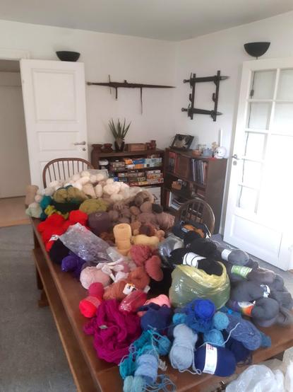 A large wooden dining table covered in yarn in many different colours.