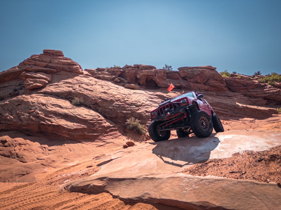 Jeep Cherokee perched on a rock with red rock in the background and blue sky.