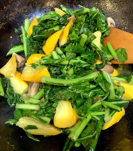 Collard Greens with yellow zucchini and mushrooms are being sautéed in a wok.