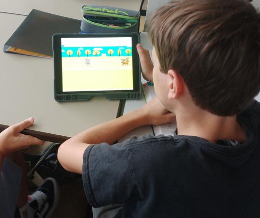 iPad mit einem Bildschirm, der zwei Pferde auf einer Rennstrecke zeigt, davor ein Schüler.