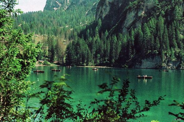 Ruderboote mit Besuchern im grünen Wasser des Pragser Wildsees in Südtirol. Im Hintergrund rechts steil aufragende Berge. Links Wald und ein Stückchen Himmel. Farbfoto mit starker Betonung der Grüntöne durch den verwendeten Film (Adox Color Implosion). Leica IIIg, 50 mm Summitar.
