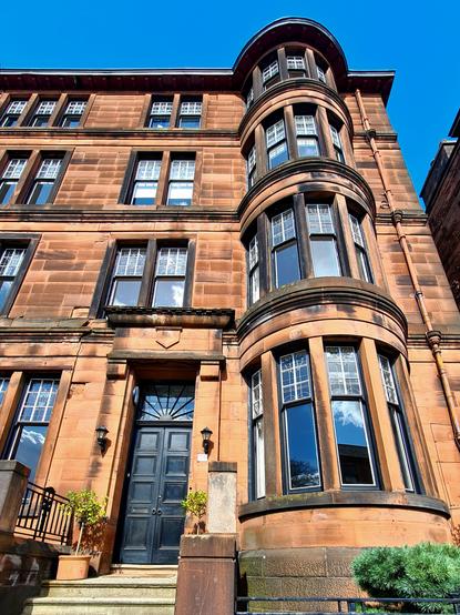 An early Edwardian Glasgow tenement made with red sandstone and featuring a  column of semi-circular bow windows.