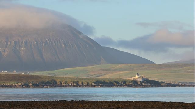 Looking out across a wide channel to distant mountains, their peaks wreathed in cloud. It's just after sunrise