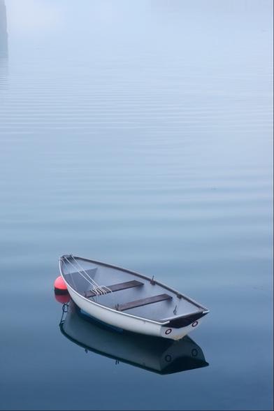 A rowing boat gently bobbing on ripples from an outgoing boat. It's misty and tinged with blue because the sunrise is happening somewhere behind thick clouds on the horizon