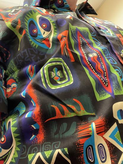 A close-up view of a colorful shirt featuring various abstract faces and patterns in bright colors on a dark background.