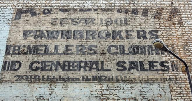 A portion of painted brick wall with layers of fading painted letters visible. Not all the words can be made out, but they included 'pawnbrokers', 'jewellers', and 'general sales'.