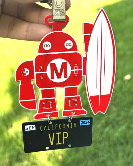 Red Makey with a surfboard on a PCB with a black California license plate that reads "VIP" hanging from Makey's feet.