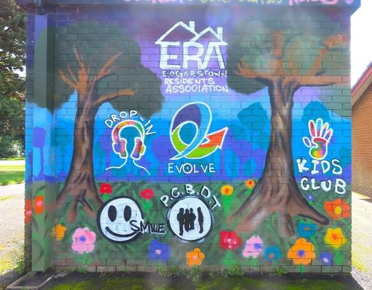 wall-painting of various emblems of community groups between two trees and flowers in grass