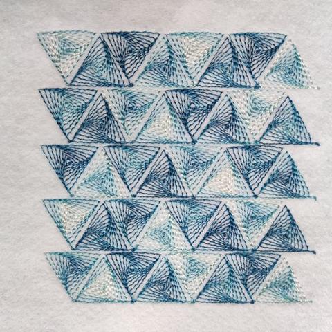 A stitched pattern made of up lines of triangles, where each triangle is is filled with a swirling pattern of smaller triangles. It uses variegated thread so the triangles appear in different colours.