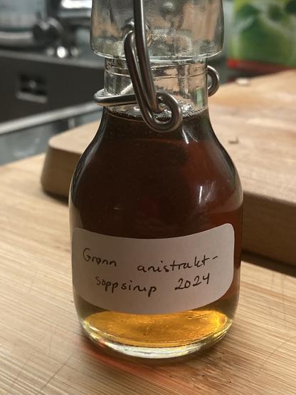 Liten flaske med gyllen sirup med merkelappen «Grønn anistraktsoppsirup 2024»