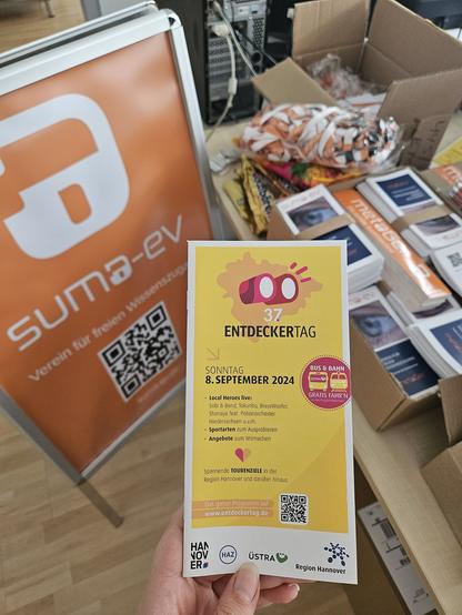 Foto von einem Flyer des 37. Entdeckertages in Hannover, einem Aufsteller des SUMA-EV und einer Menge von Goodies