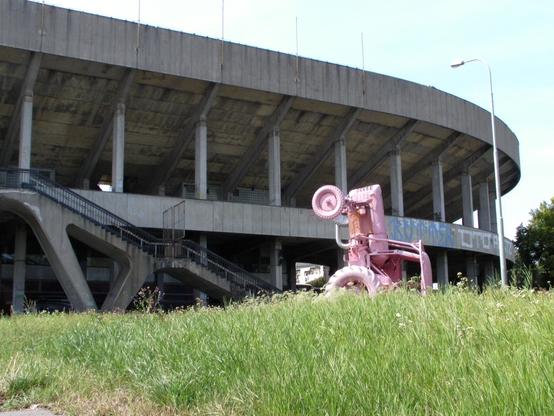 That one huge stadium in Prague with a pink painted tractor standing in front of it. The stadium is made out of concrete. The entrance stairs to it are closed off.