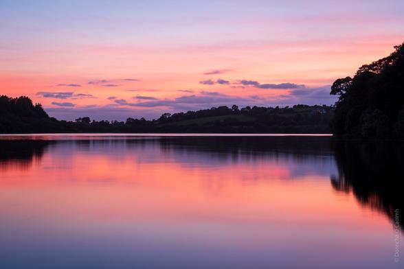 The pinks and oranges and reds of the sky after the sun has set are reflected in the water of the River Lee at Inniscarra.