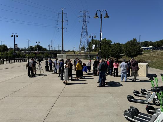 After a news conference, people standing around and having conversation at the Decatur-Federal transit stop in Denver. Again, concrete hellscape, no shade.