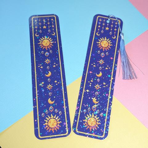 Pixel art bookmark with suns with faces, moons, stars, and crystals with holographic stars laminate. One of the bookmarks has a tassle.