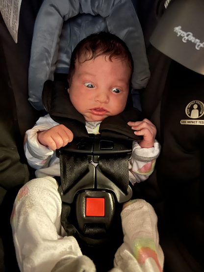 An infant in a carseat looks to the right with wide eyes.