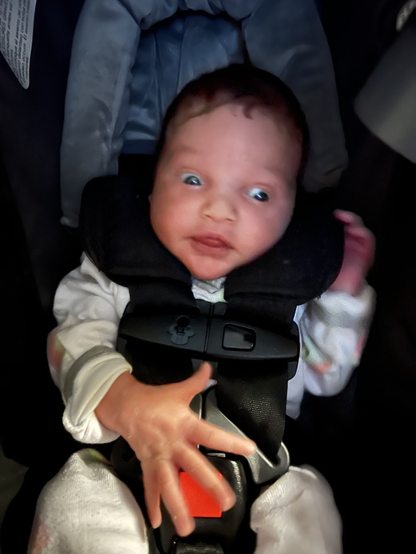 An infant in a carseat with wide-open eyes, open mouth, and waving hands.
