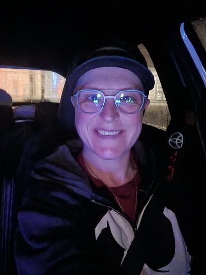 A selfie of a person, sitting in a car during night time. Smiling at the camera, but feeling rather defeated.
