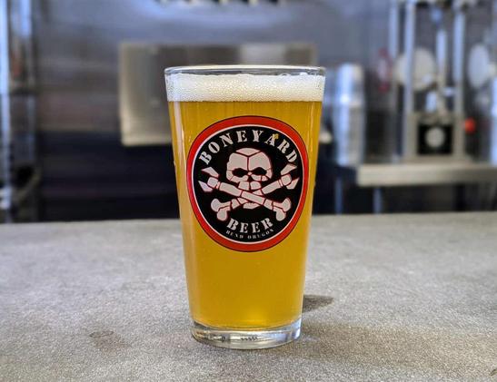 A pint of Yokozuna IPA from Boneyard Beer of Bend, Oregon. It's a citrus-infused India pale ale, and the glass showcases the round "Boneyard Beer" logo, featuring a skull and crossbones where the two crossbones are also wrenches.