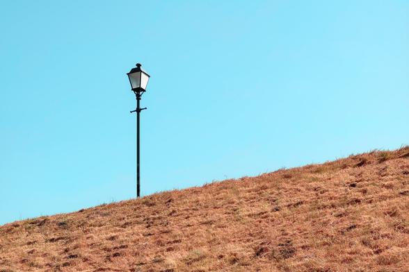 A lone lantern standing in front of blue sky. Below it, there's a field of yelow-ish dry grass (it was like that in reality but the color preset amplified that effect quite a lot).