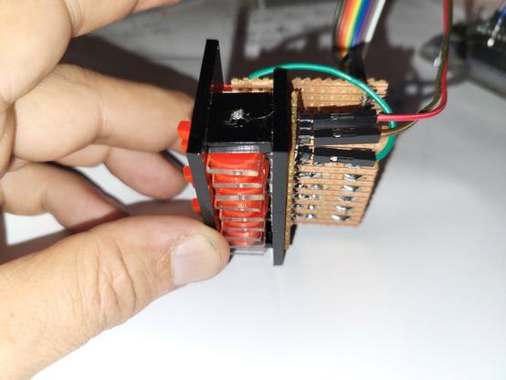 Fingers holding a black acrylic construction, red switches in a frame on the left with vero board and connectors on the right