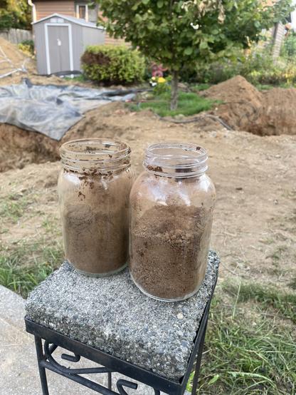 Two jars stand on top of a small platform. One is narrow one is wide. Behind them is the yard with a hole on both sides.