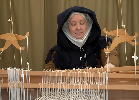 A woman in medieval attire, doing a weaving loom demonstration.