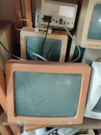 A pile of five computer terminals. The one in the foreground has a brown bezel and may date from the 1970s.