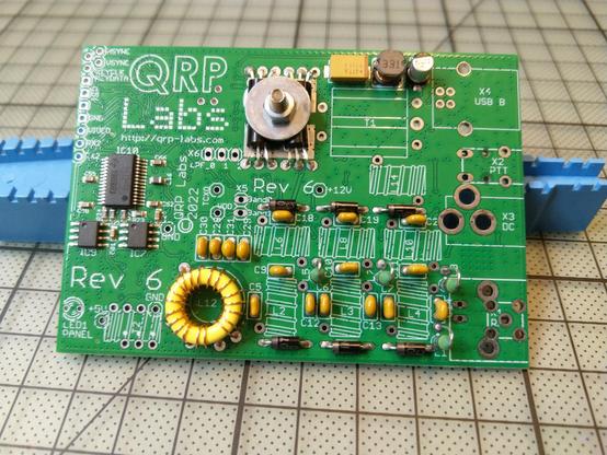 A green circuit board for the QDX transceiver with some components soldered on, others still missing.