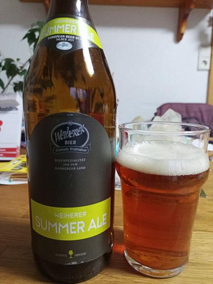 Auf einem Tisch steht ein Glas mit braunem klarem Bier und daneben die passende Bierflasche