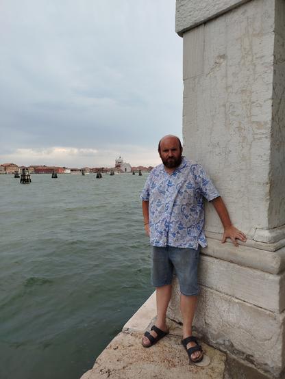 Veneziako Doganako puntan nago, udako outfitarekin Giudecca kanaleko uren ondoan, pose jarrerarekin.