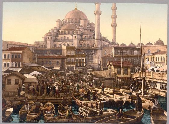 This image is a postcard depicting the bustling life of Istanbul's Eminönü bazaar and Yeni Cami (New Mosque) around 1890-1900. The scene is vibrant with people engaged in various activities, creating an atmosphere of liveliness and commerce. The buildings have distinct Ottoman architectural features, such as the domes and minarets that are characteristic of this style. The color palette consists mainly of earth tones, providing a sense of warmth and history to the scene.