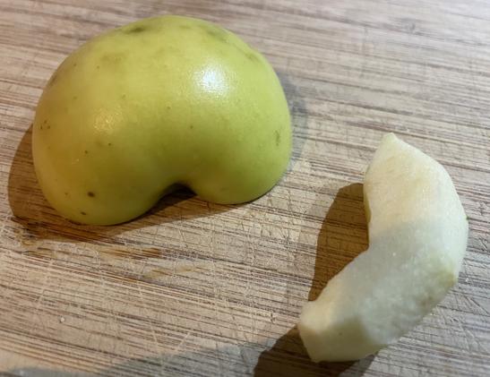 Photo of a medium/small yellow/green skinned apple halved on a wooden chopping board, with a skinned segment to the right.