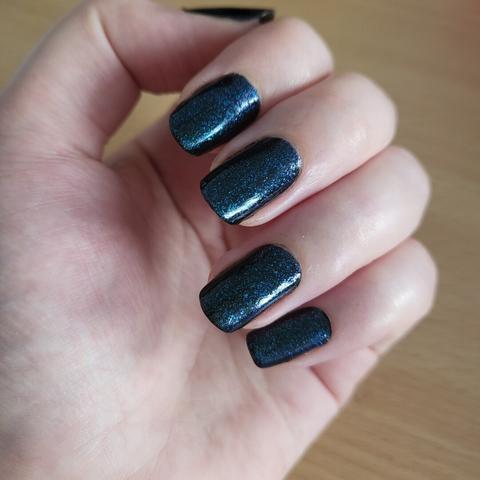 manucure noire avec un top coat pailleté bleu pour un effet galaxy glossy