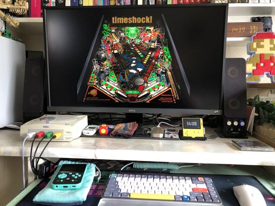 A desk with a Sega Dreamcast on it with Pro Pinball Trilogy playing on screen.