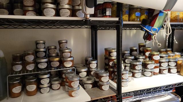 Photo of two big rows of shelves packed with jars of canned foods with oval labels.