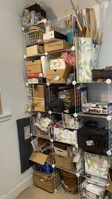 A shelving unit filled with various craft supplies, boxes, and organization baskets. Items include paints, fabrics, tools, and other materials, with labeled containers for easy access in the corner of my craft room.