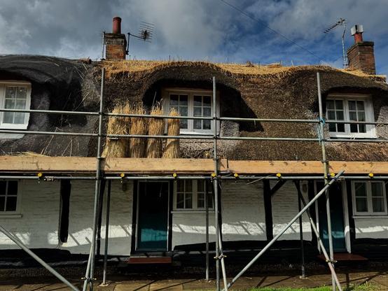 A photo of a row of three traditionally thatched terraced cottages in Hertfordshire village, under a stormy and bright late summer sky