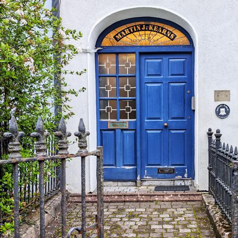 Simple blue door with double panel of side lites on the left. The fanlight is lit from within and reads "Martin J. Kearns"