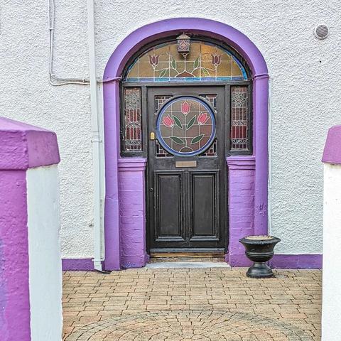 Black door with a bright purple frame. The door is decorated with elegant stained glass in a floral motif.