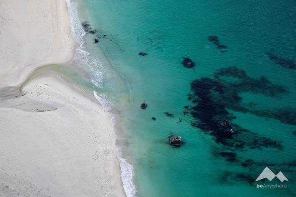 White sandy beach on the left, turquoise-coloured water with a few dark stones on the right.