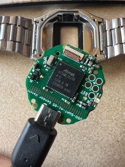 Das Herz der Sensorwatch: zu sehen ist das grüne Board an einem Micro-USB-Kabel. Im Hintergrund liegt das Gehäuse einer Casio A163.