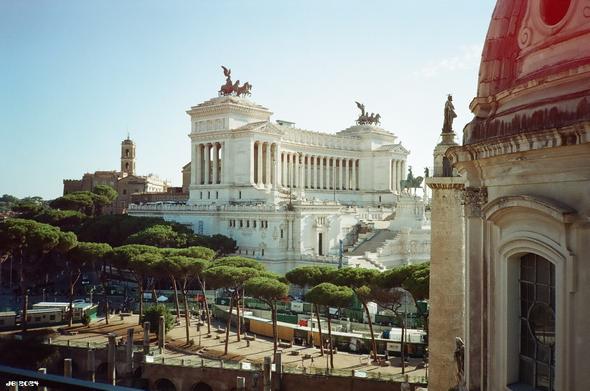 Farbfoto, aufgenommen von der Dachterrasse eines Hotels im Zentrum von Rom mit Blick auf das Denkmal für Viktor Emmanuel II in Bildmitte und die Gegend um die Via dei Fori Imperiali, an der gerade emsig gebaut wird. Rechts ein Teil der Kuppel der Chiesa del Santissimo Nome di Maria al Foro Traiano. Olympus XA auf Kono Mirage-Film.