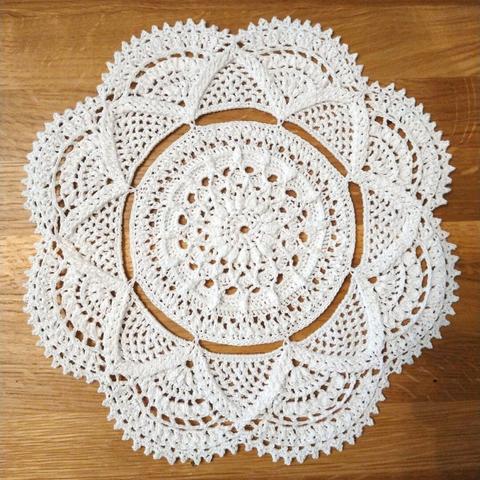A round doily, crocheted from thin white thread. The pattern has two main sections, inner and outer, joined only by a few stitches to give a pleasing circular gap between the two. The inner section uses bobble stitches for a textured effect, while the outer section is eight repeats of the lace with scalloped edges to the outside.