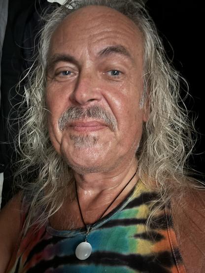 Selfie of a man with long white hair and a rainbow tie-dye shirt, wearing a beautiful selenite necklace from the street fair. Its crystals grow so straight that when polished, selenite has strong chatoyancy.